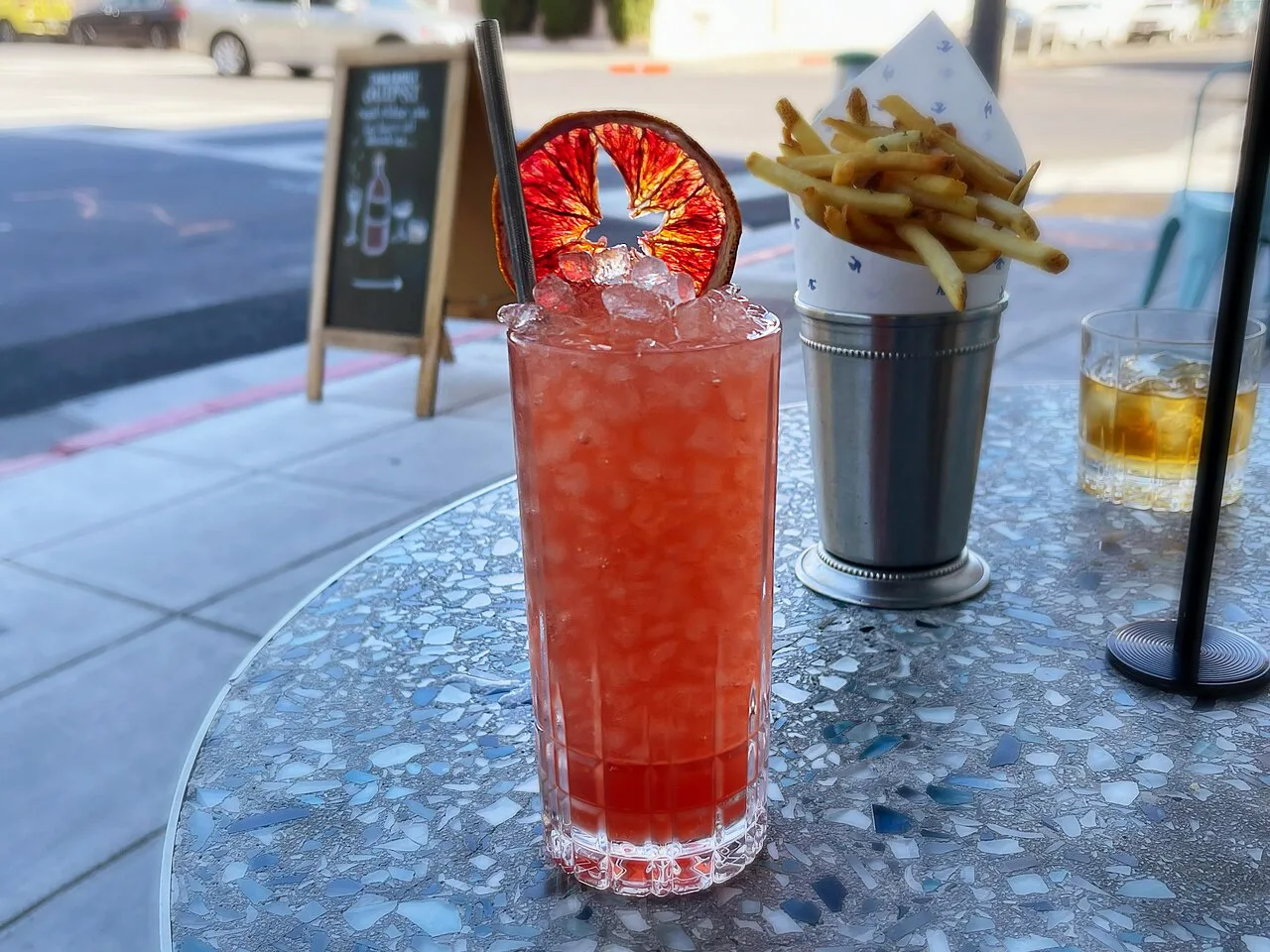 A red spritz with a bowl of chips on a café table.