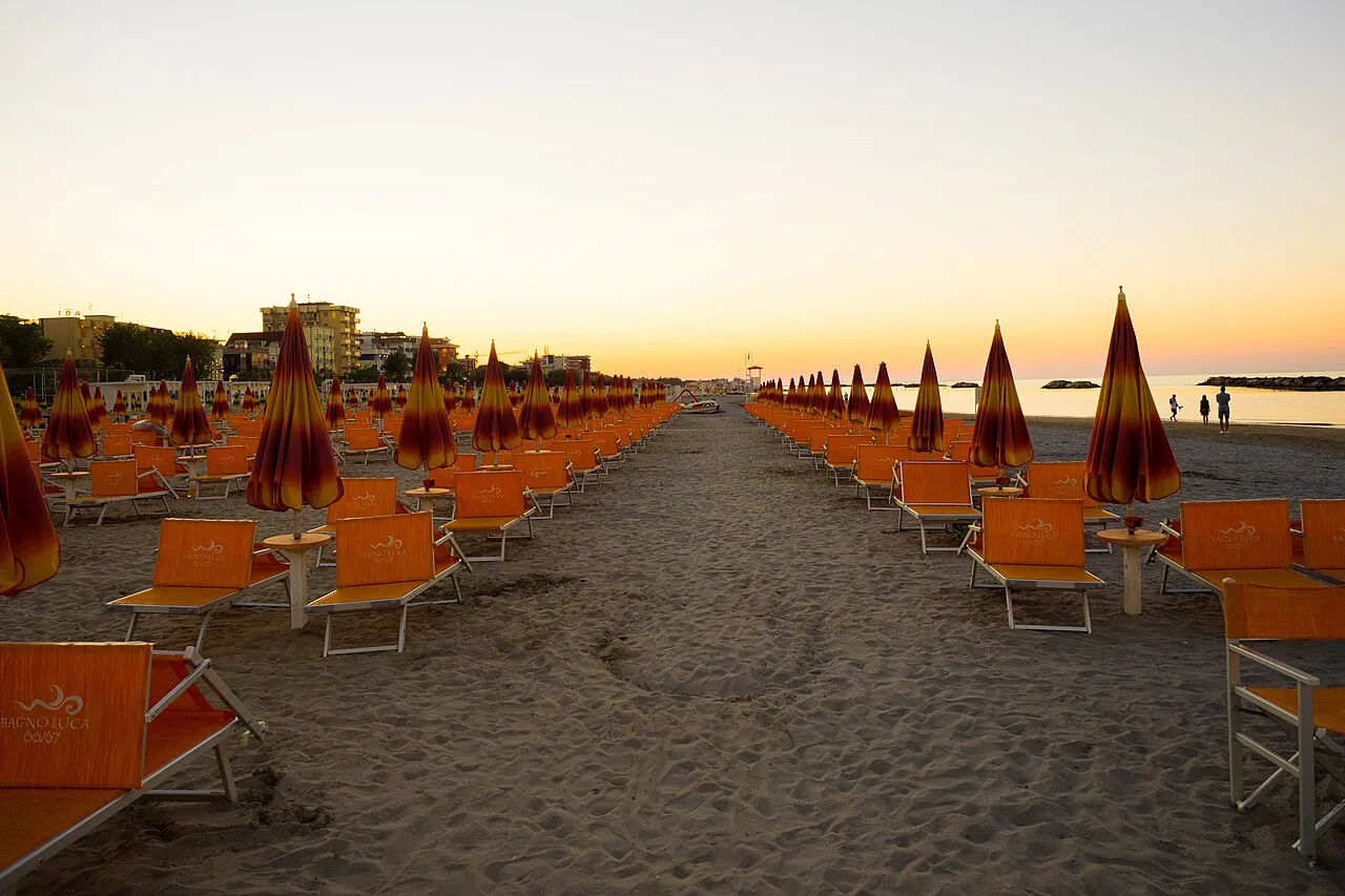 Rimini beach at sunset, lined with umbrellas.