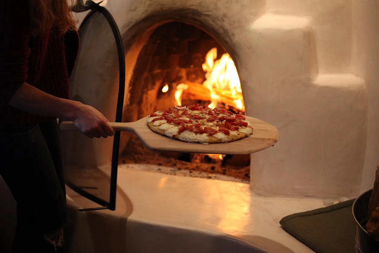 A pizza going into a wood-fired oven.