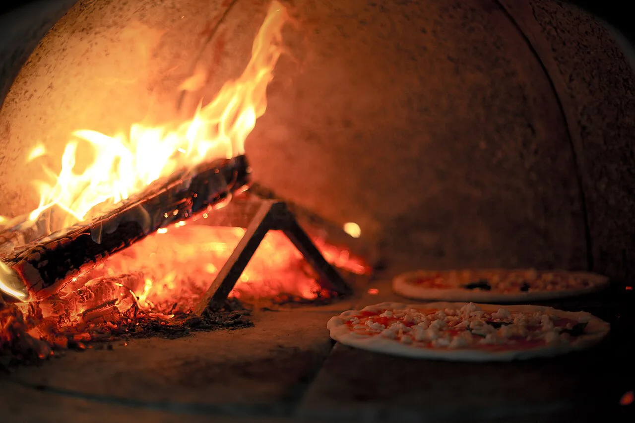 A wood-fired brick oven with pizzas baking.
