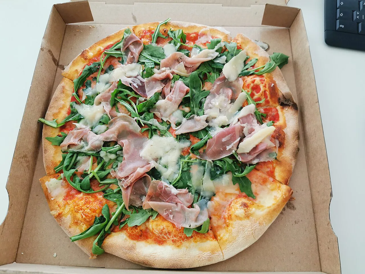 Takeaway pizza with ham and rocket.