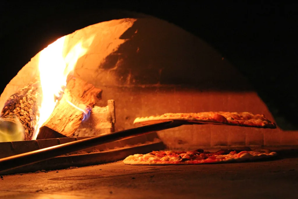 Pizzas baking in a wood-fired oven at a pizzeria near Verona.