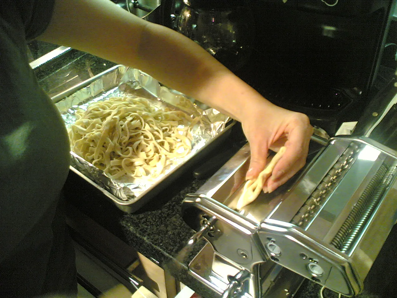 Fresh pasta being rolled through a pasta machine.