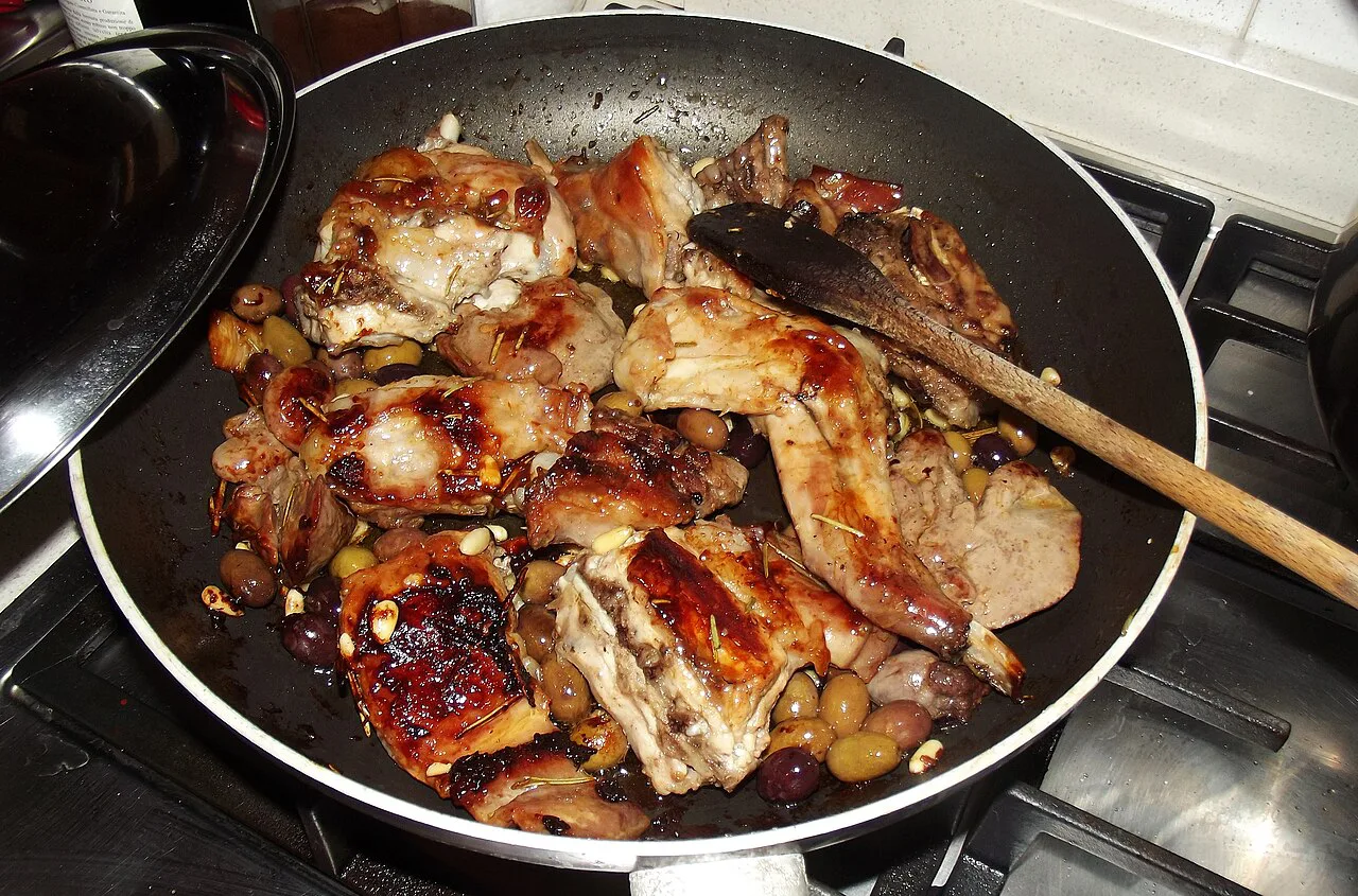 Rabbit with olives and pine nuts cooking in a pan.