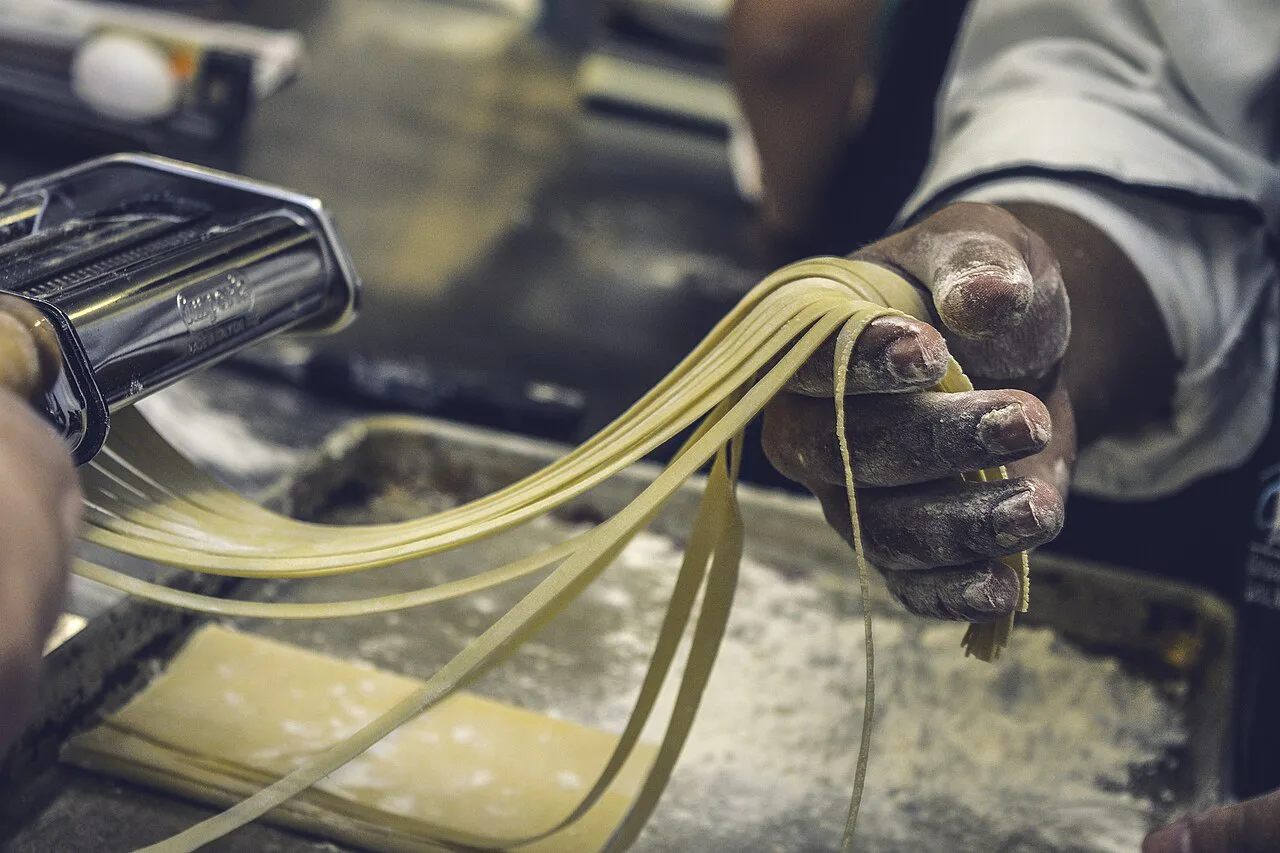 Hands feeding dough through a pasta machine.