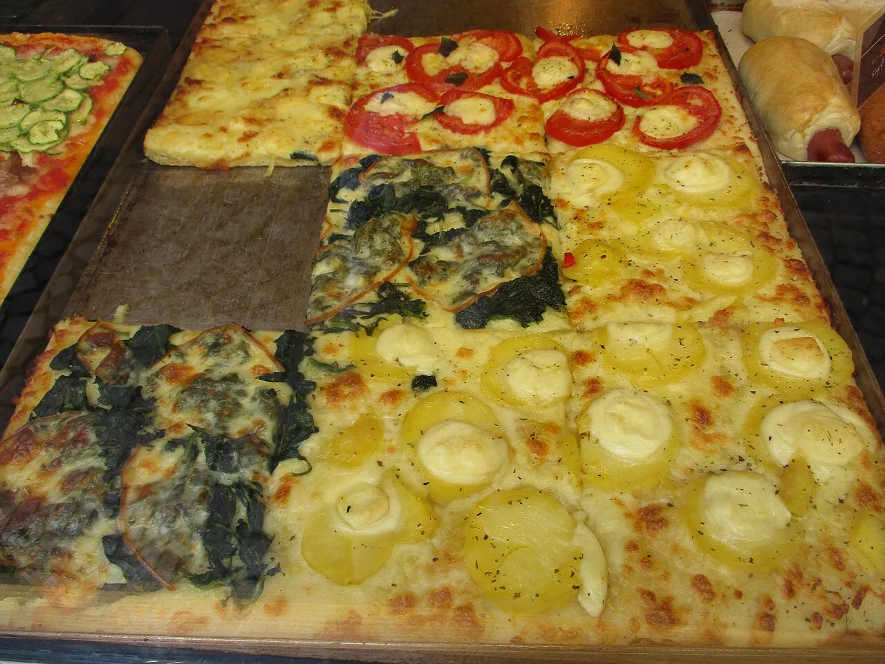 Trays of Roman pizza with varied toppings.