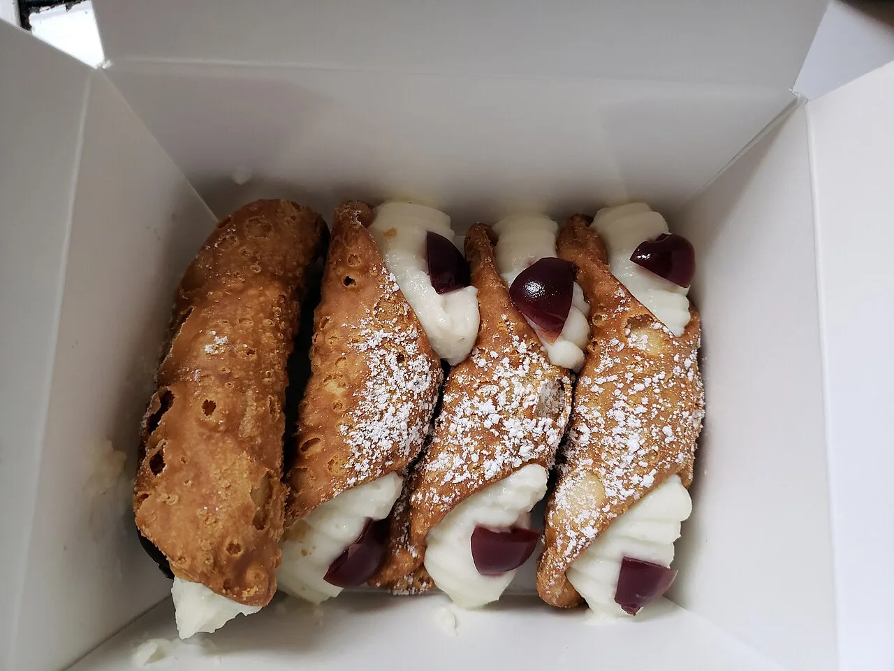 Cannoli in a box dusted with icing sugar.
